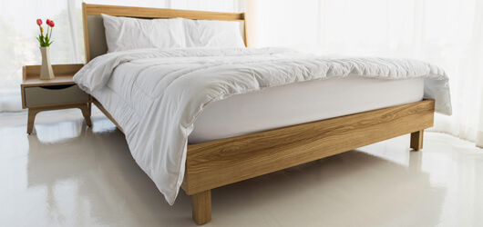 The Wooden Bed Is Laid With White Sheets In Empty Room Surrounde